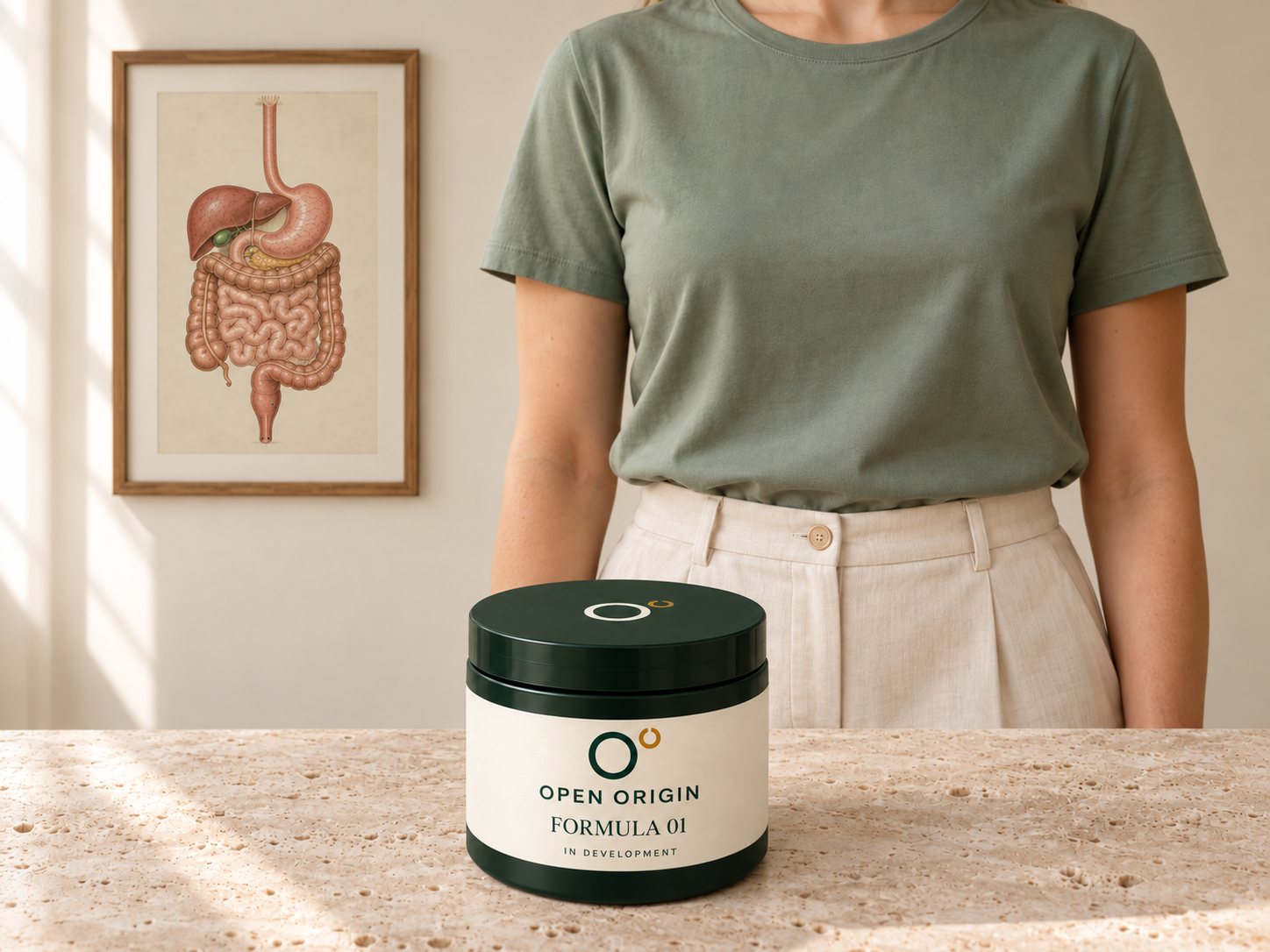 Open Origin Formula 01 concept jar on a travertine counter in front of a person in a sage shirt, beside a framed vintage digestive-anatomy print.